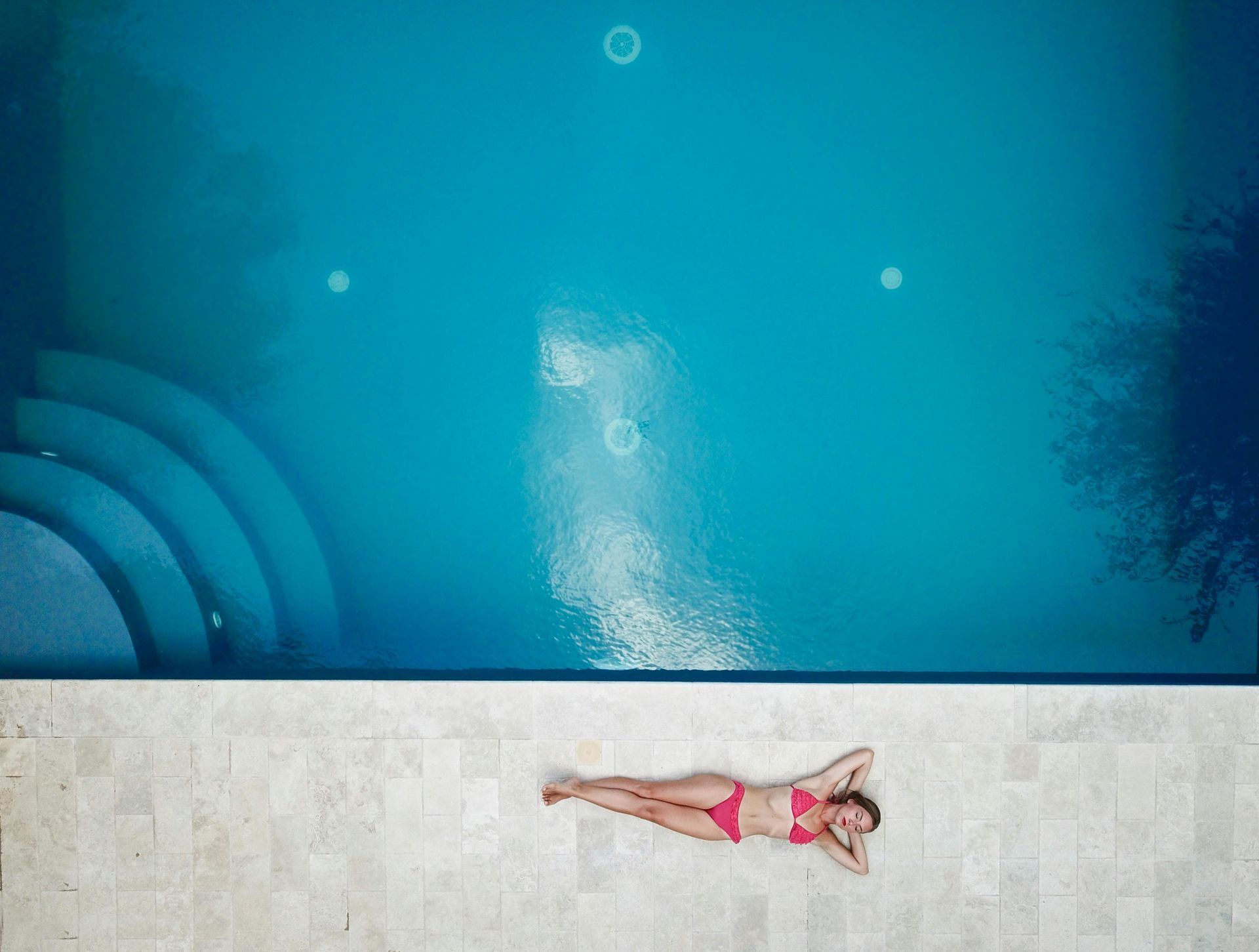 Woman in pink swimsuit sunbathing on the edge of a turquoise pool.