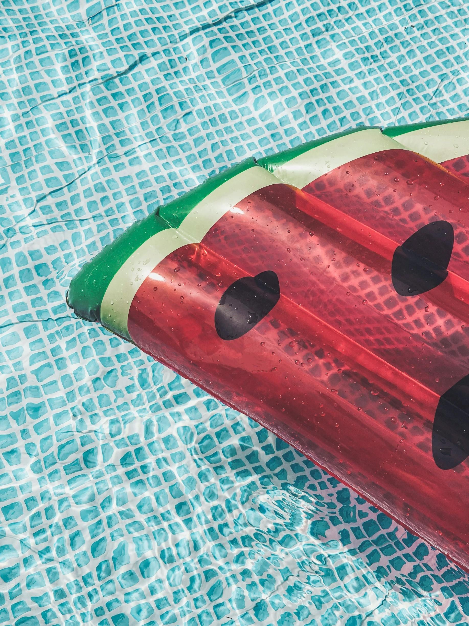 Watermelon-shaped pool float in a blue tiled pool; the float is red with black