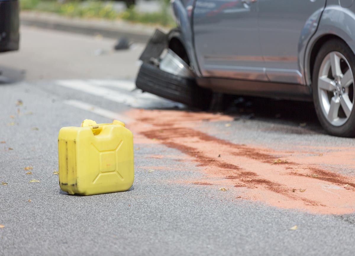 A yellow gas can is sitting on the side of the road next to a car that has been involved in a car accident.