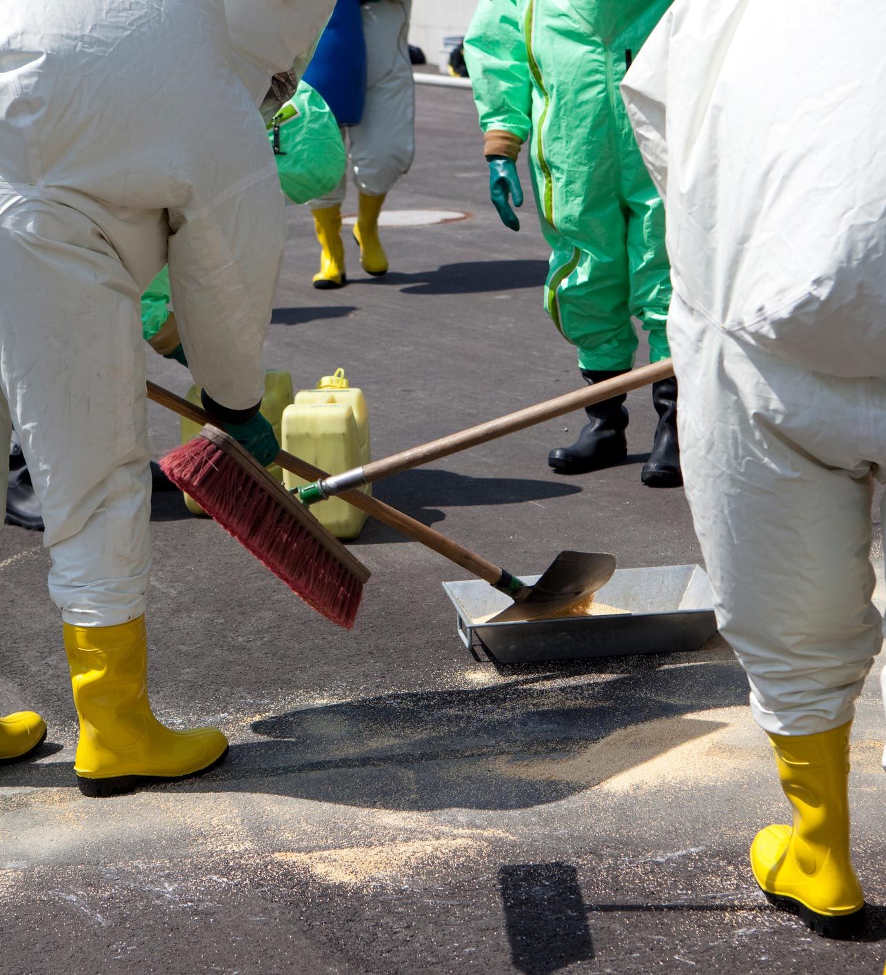A group of people wearing white suits and yellow boots are cleaning the ground
