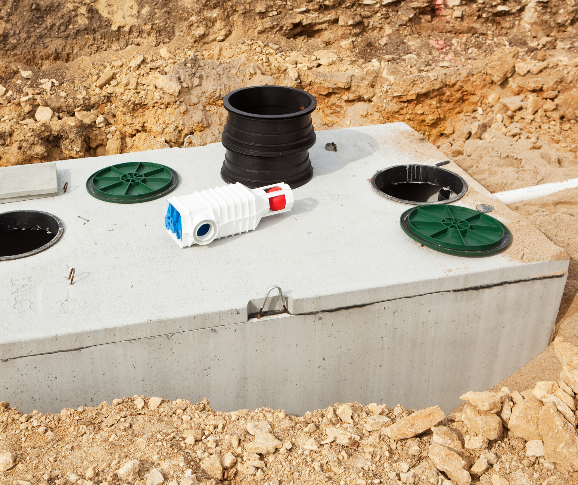 Concrete underground tank with black pipe openings, green covers, and a white PVC fitting at a construction site