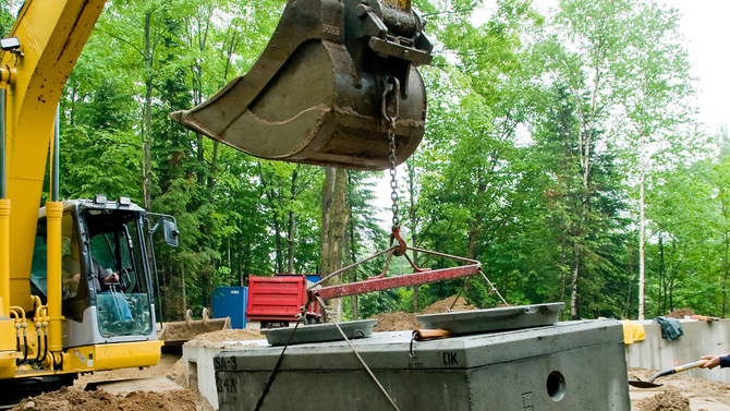 Excavator lifting a bucket over a concrete site in a wooded area