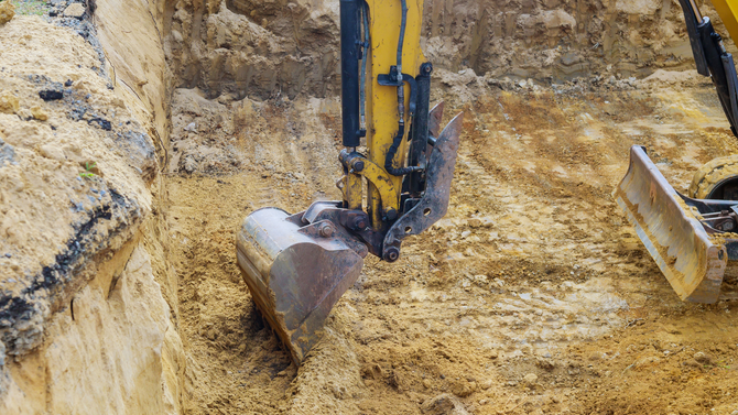 Excavator bucket digging yellow soil in a trench at a construction site