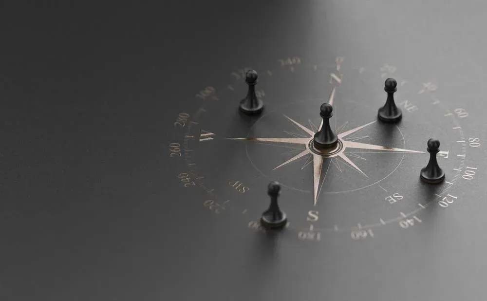 A compass with chess pieces on it on a black surface.