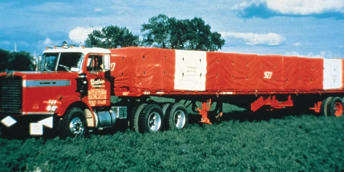 A red and white semi truck is parked in a grassy field.