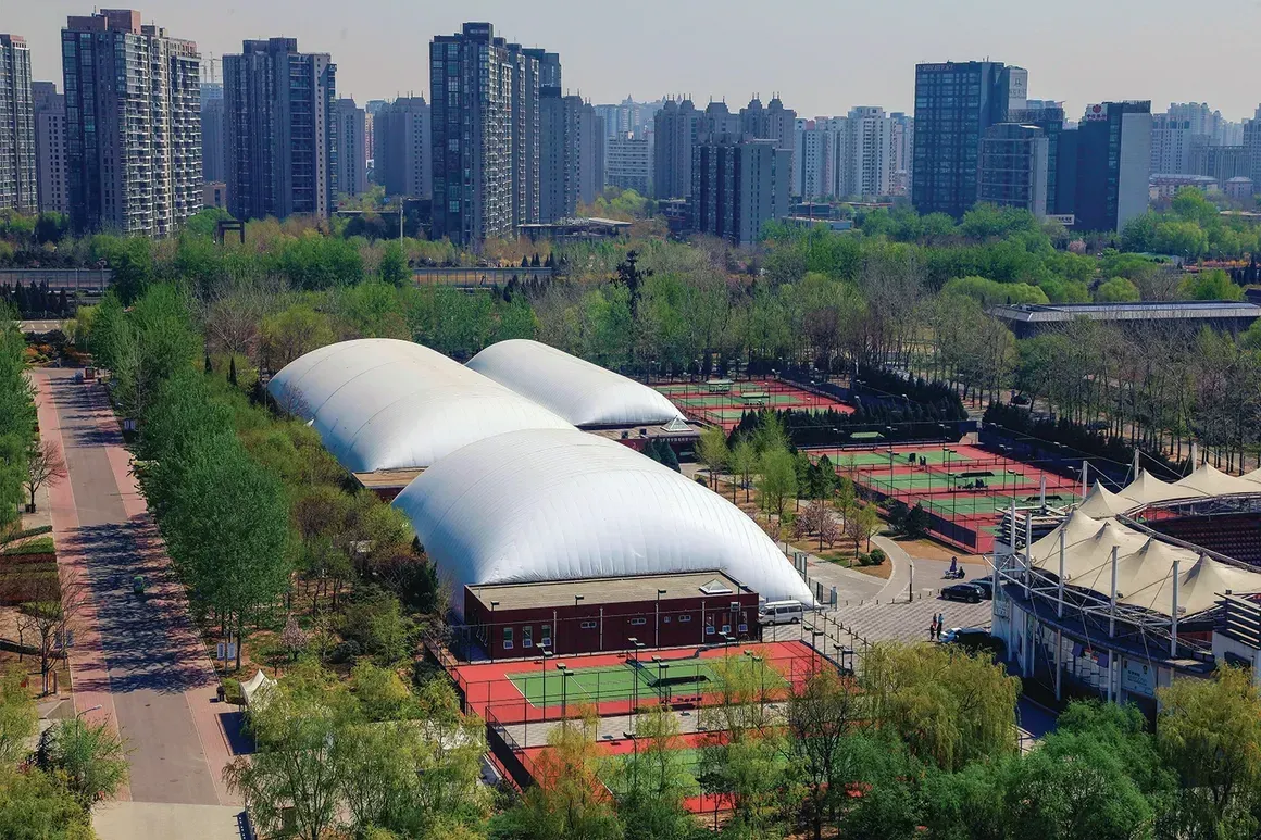 An aerial view of a tennis court in a park with a city in the background.