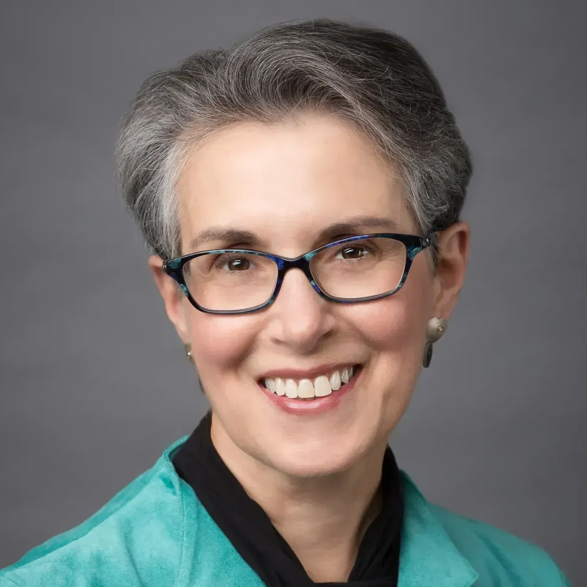 A woman wearing glasses and a green jacket is smiling for the camera.