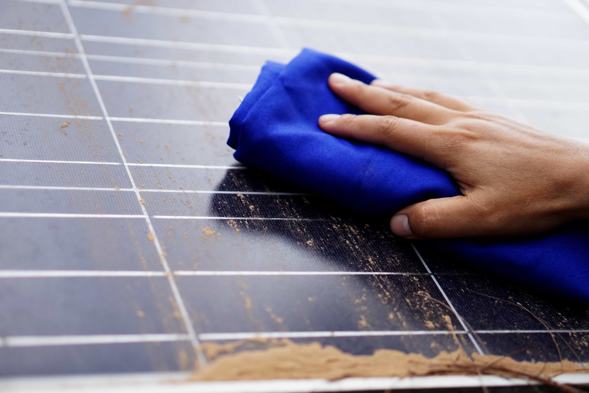 Hand wiping dust from a dark solar panel with a blue cloth