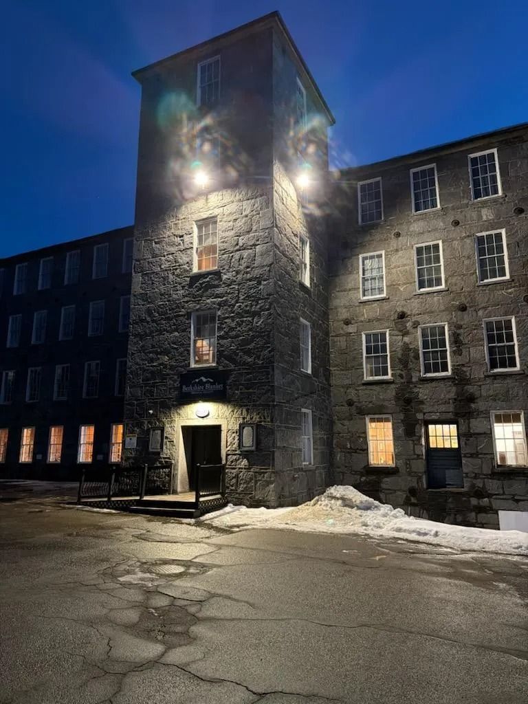 Stone building tower lit at night beside a dark residential block, with snow on the ground.