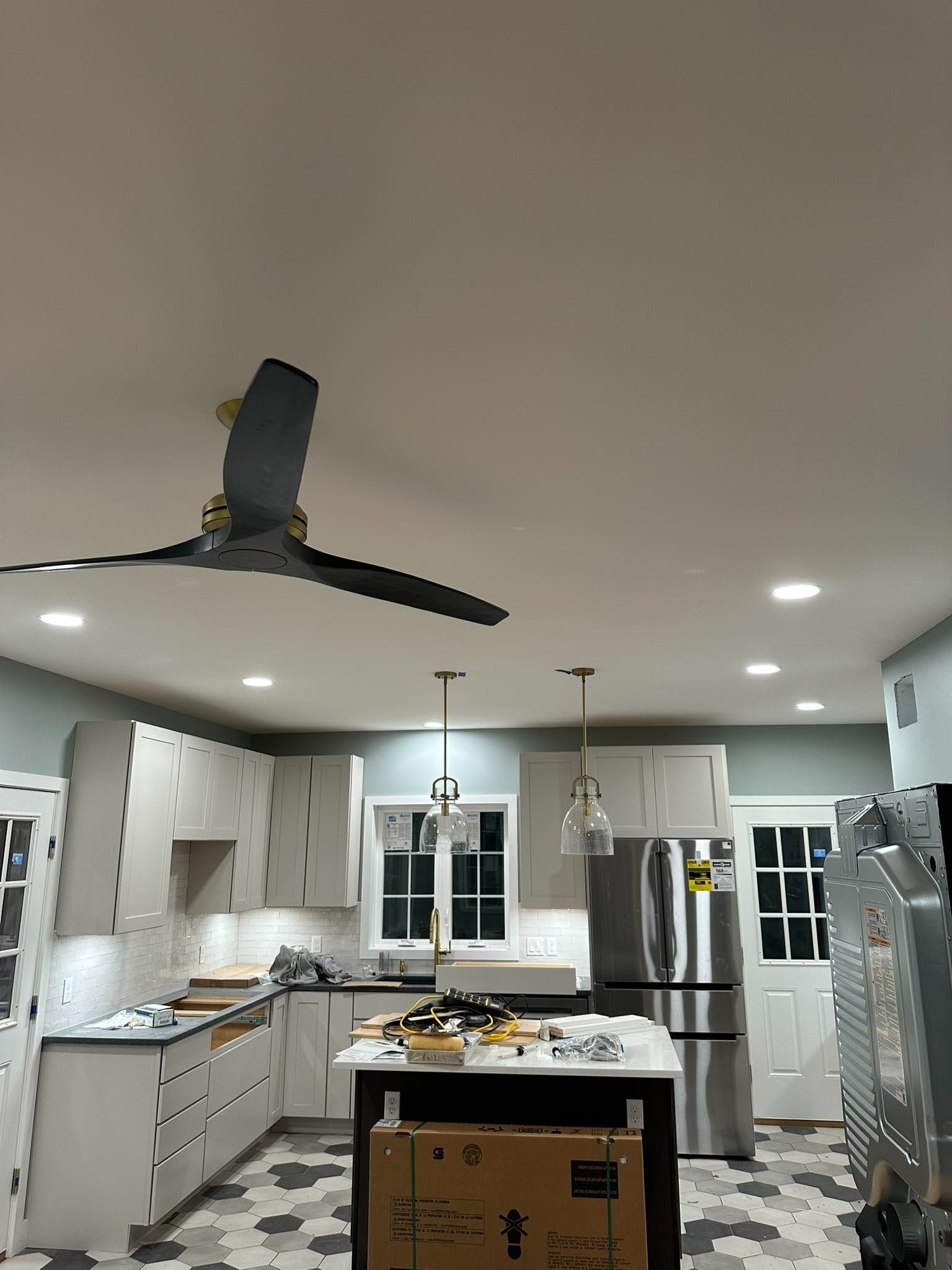 Bright modern kitchen with white cabinets, island, stainless fridge, and ceiling fan under recessed lights