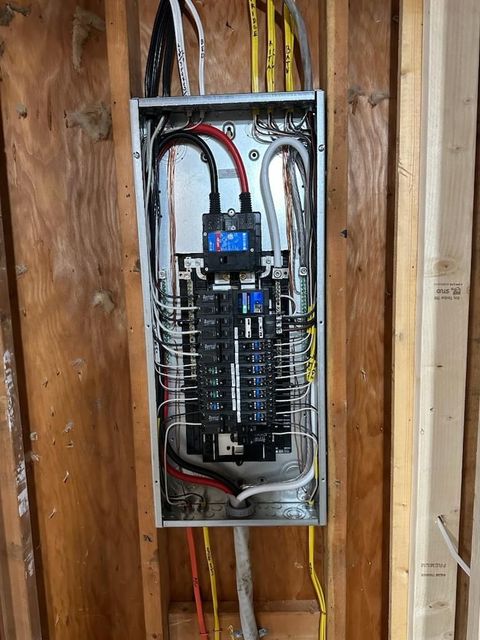 Open electrical breaker panel mounted in unfinished wood wall with exposed wiring