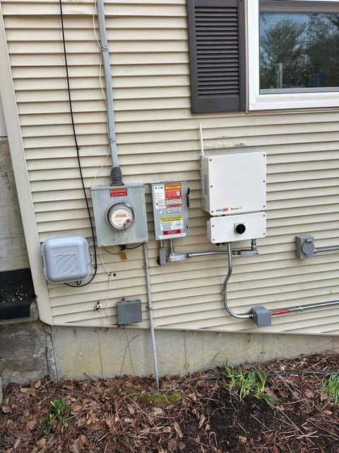 Outdoor house utility meters and electrical boxes mounted on beige siding beside a window.