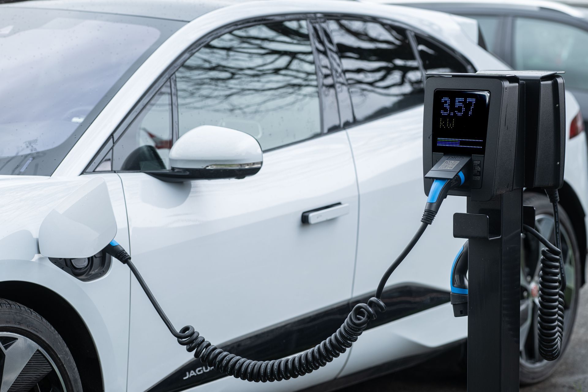 White electric car charging at a station with a cable connected to the front port