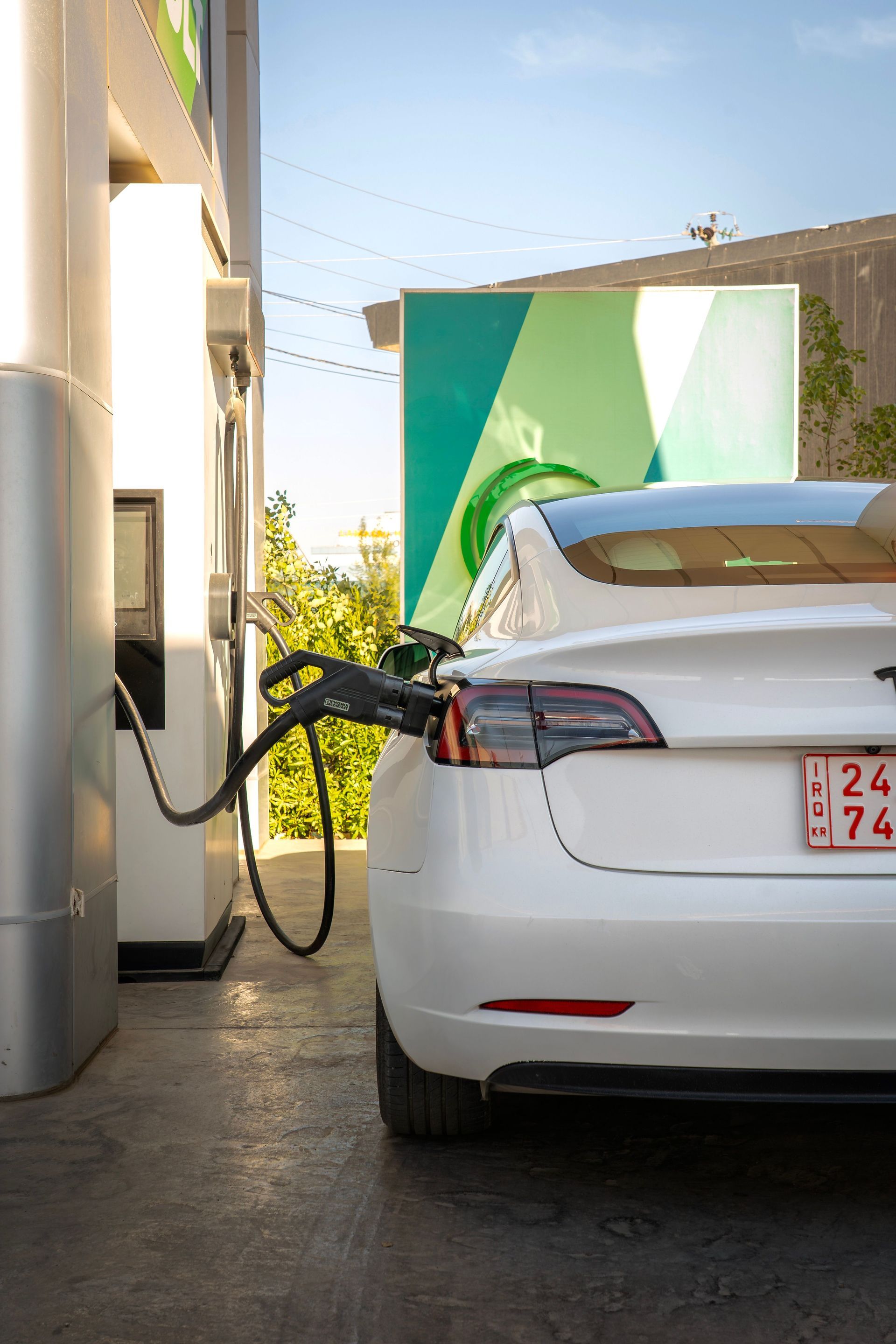 White Tesla charging at a gas station pump, rear view with hose connected.