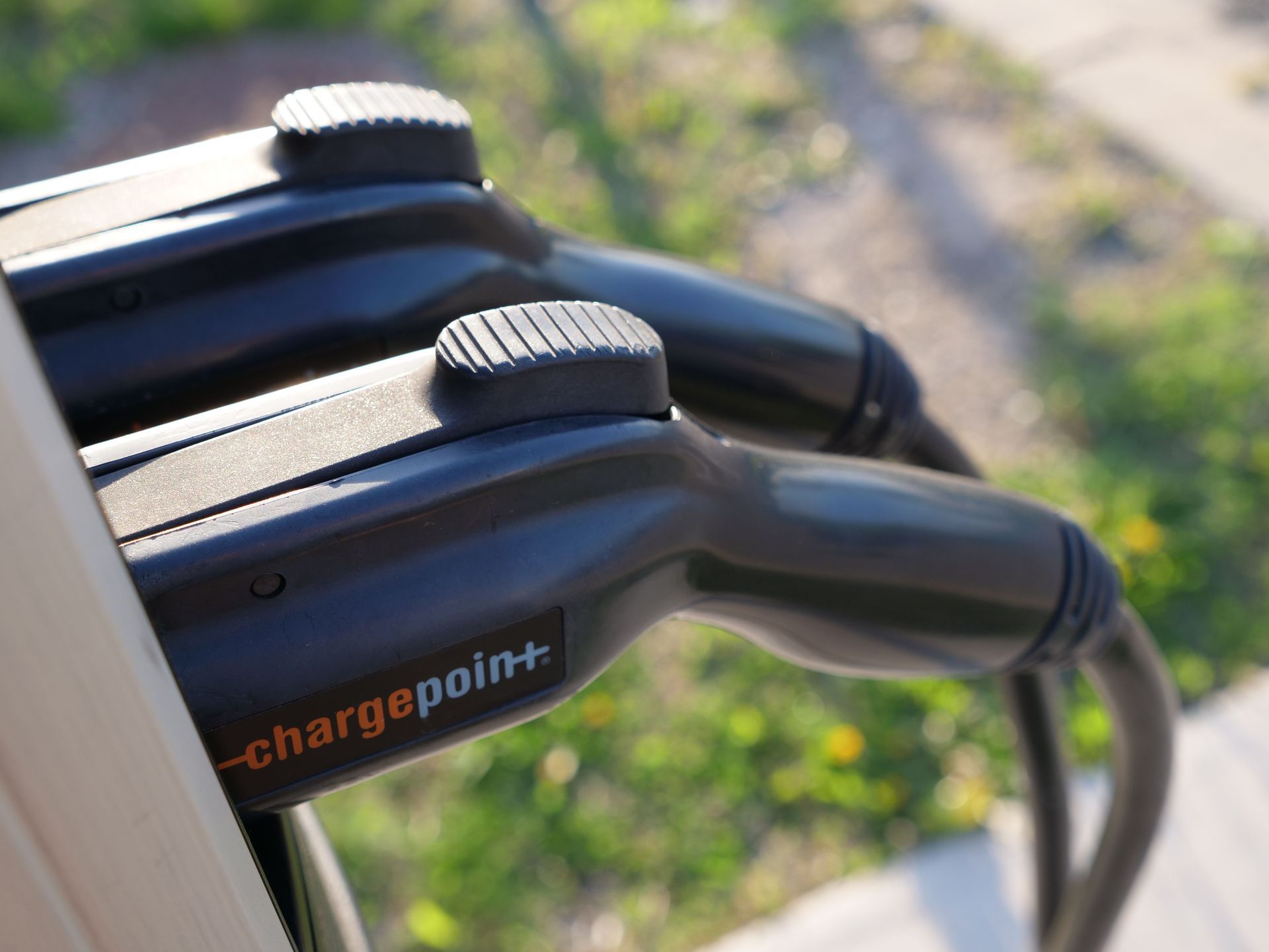 Two black EV charging plugs with orange ChargePoint logo clipped into a charging station outdoors
