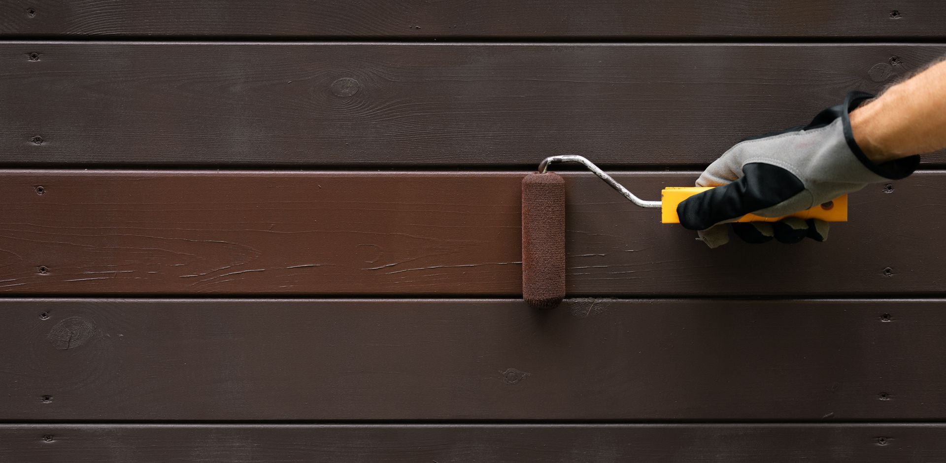 A person painting a wooden surface with a brown paint roller.