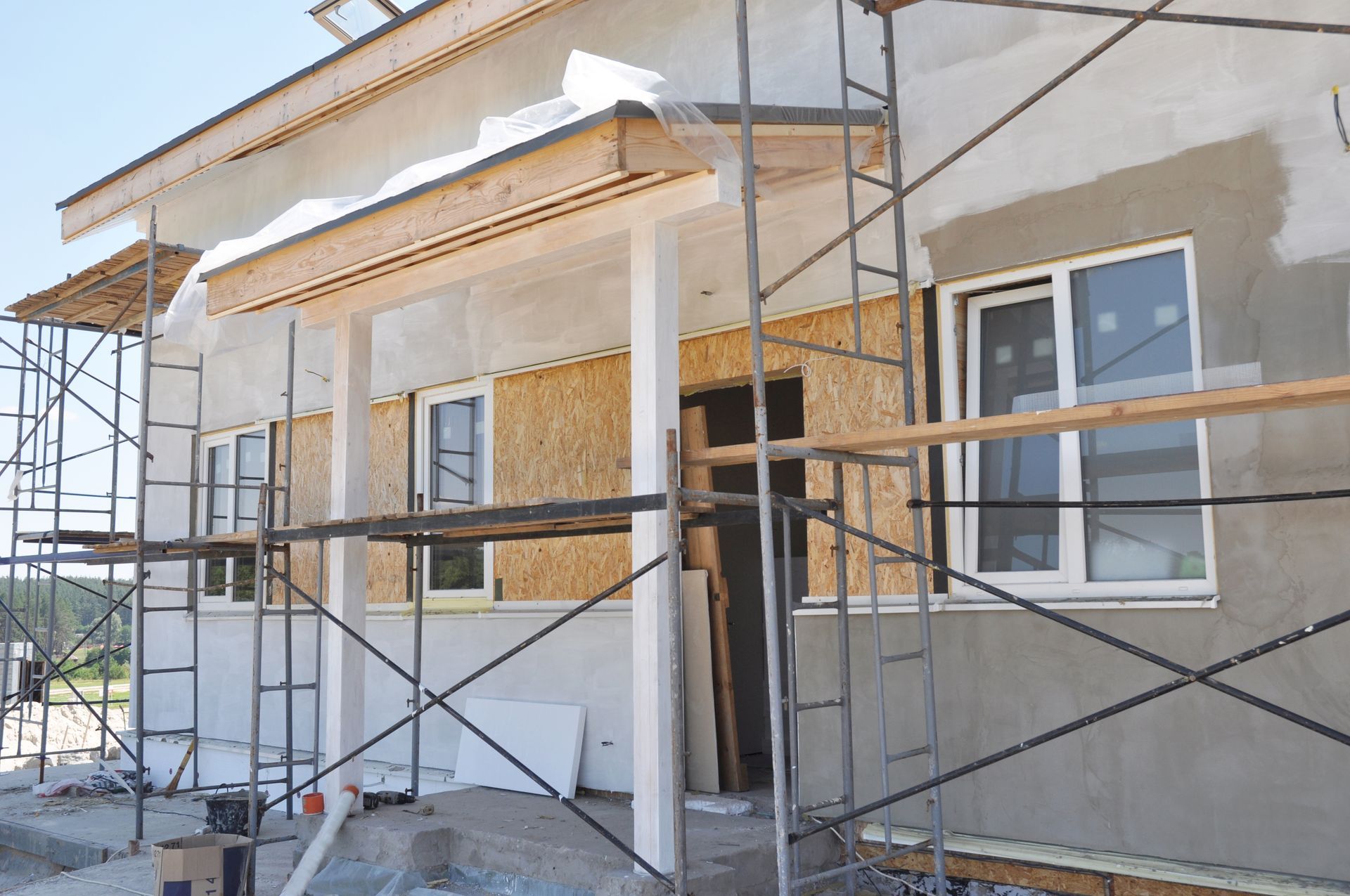 House under construction, exterior view with scaffolding, windows, and unfinished stucco.