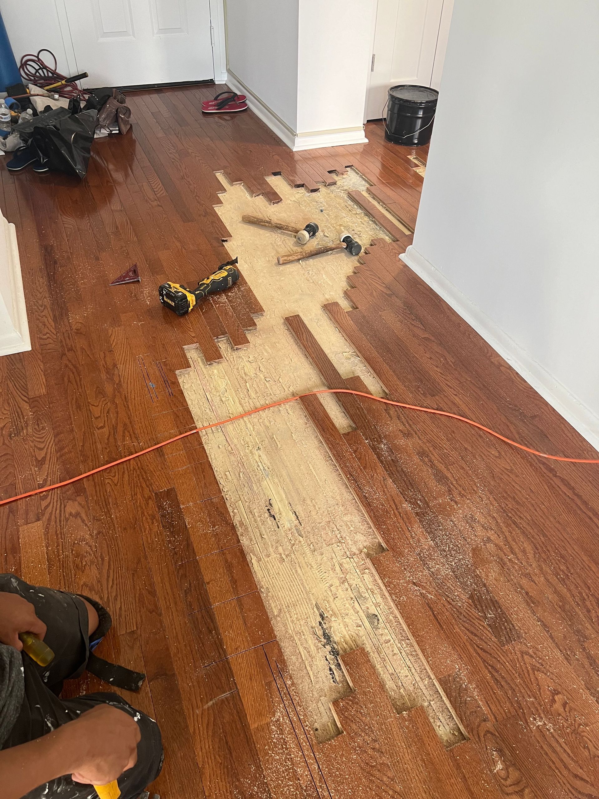 Wood floor being refinished, showing exposed wood, tools, and sawdust.