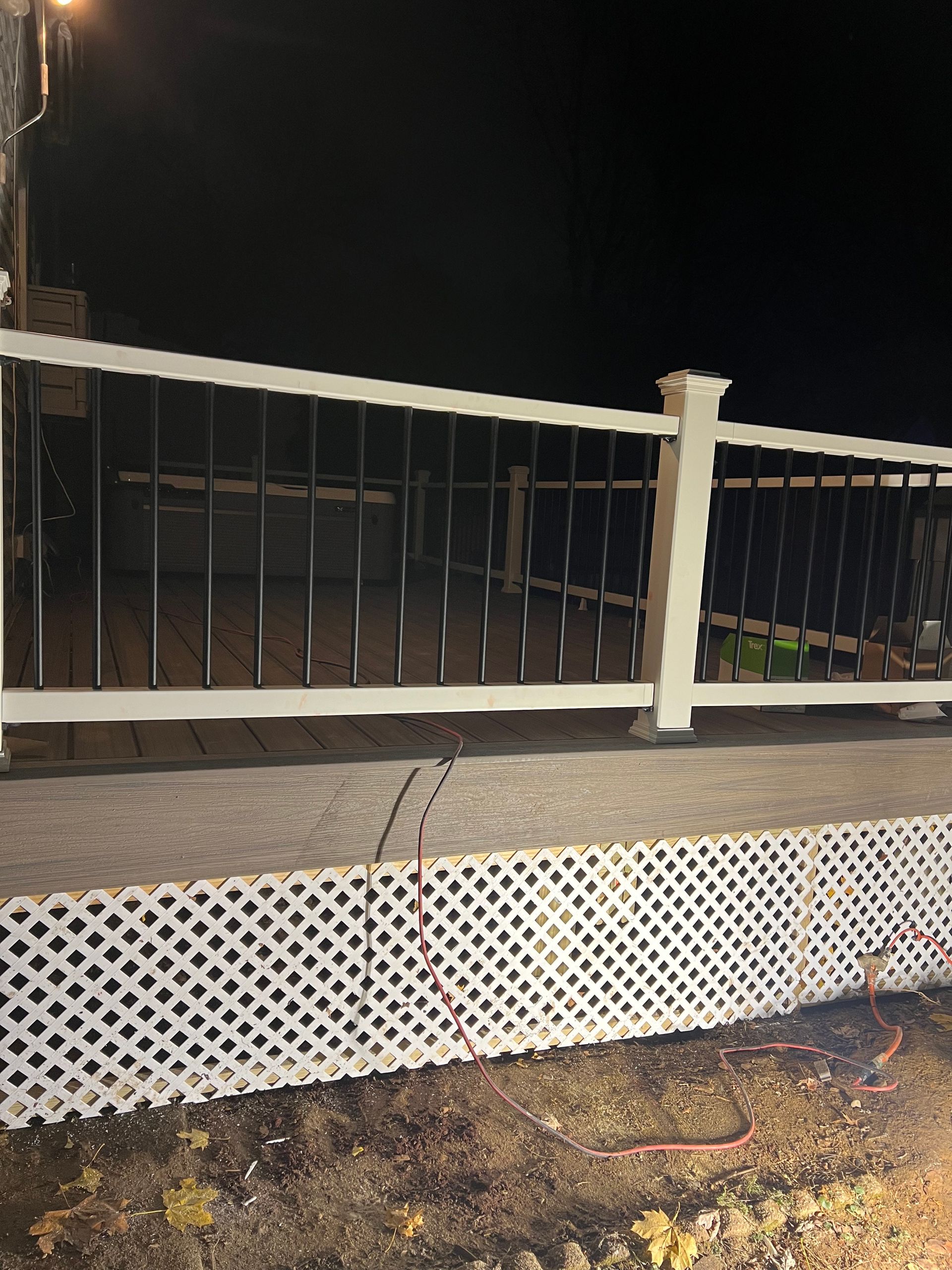 White and black fence with lattice base, in front of a porch, at night.