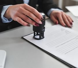 Hands stamping a document with a black self-inking stamp on a desk