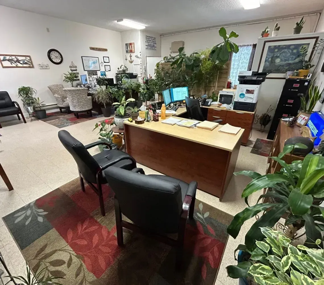 Office with a wooden desk, black chairs, potted plants, and wall decor in a bright room.