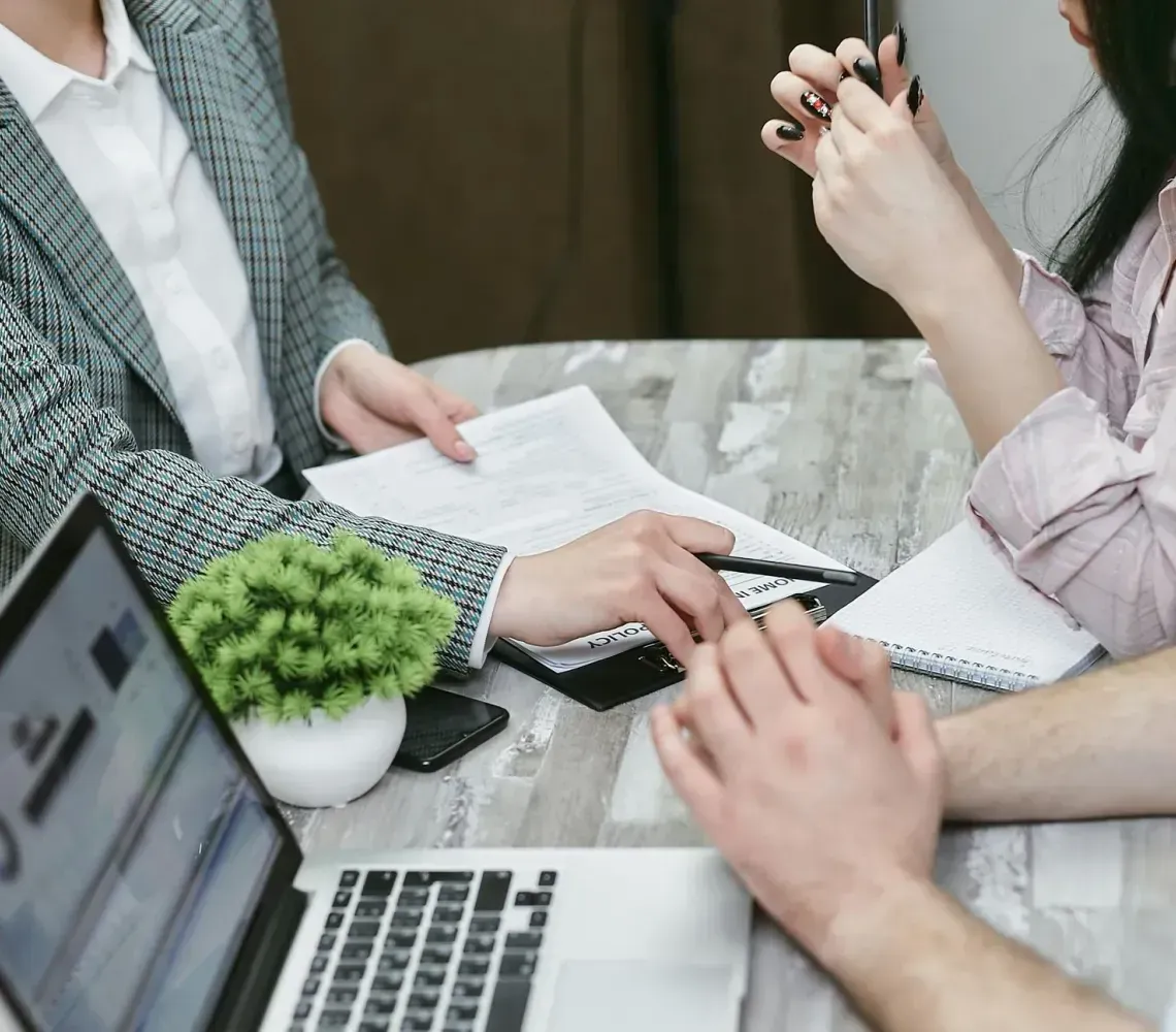 Three coworkers reviewing documents at a table with a laptop and notebook in a meeting room