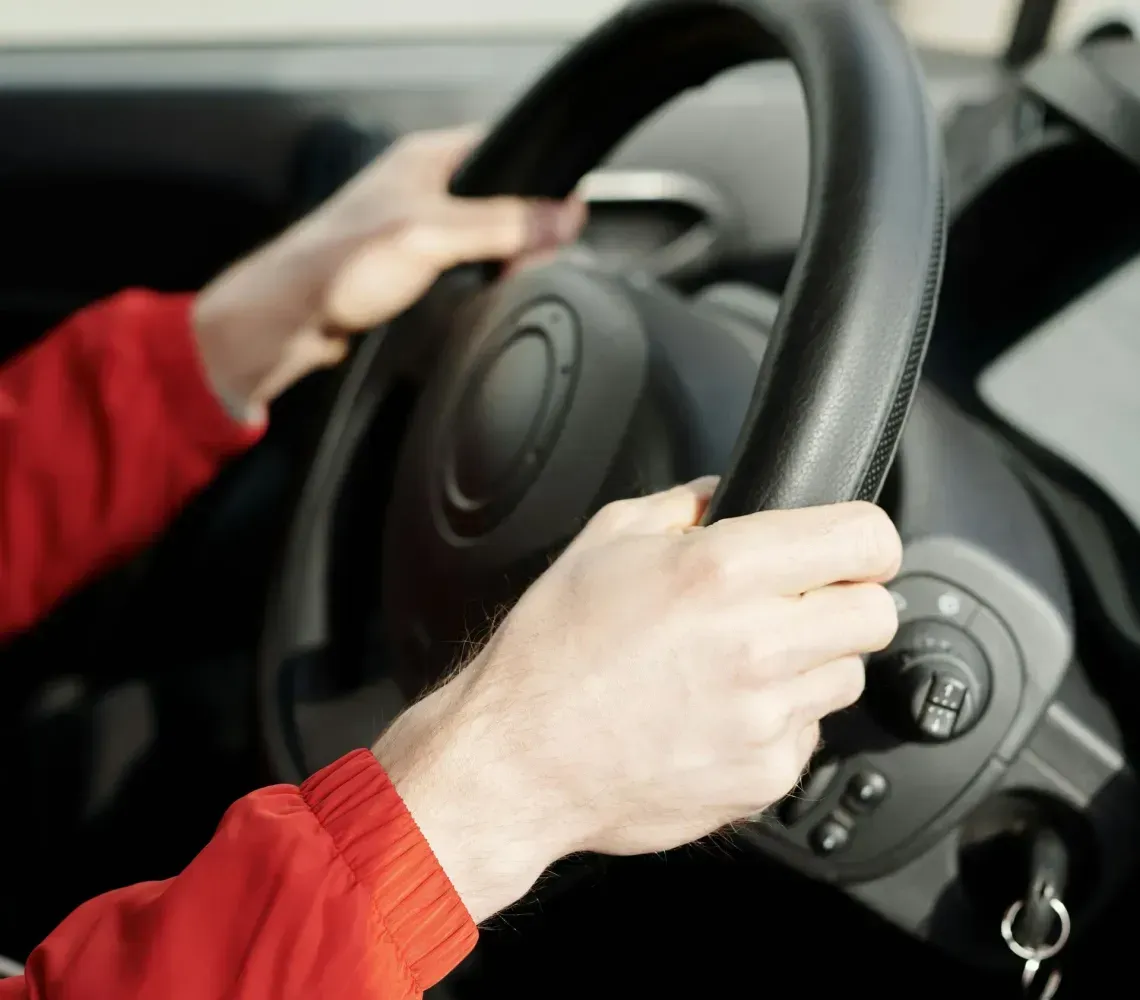 Hands gripping a black steering wheel inside a car, with a red sleeve visible.