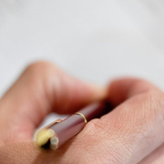 Hand holding a purple lipstick with a gold tip on a light background
