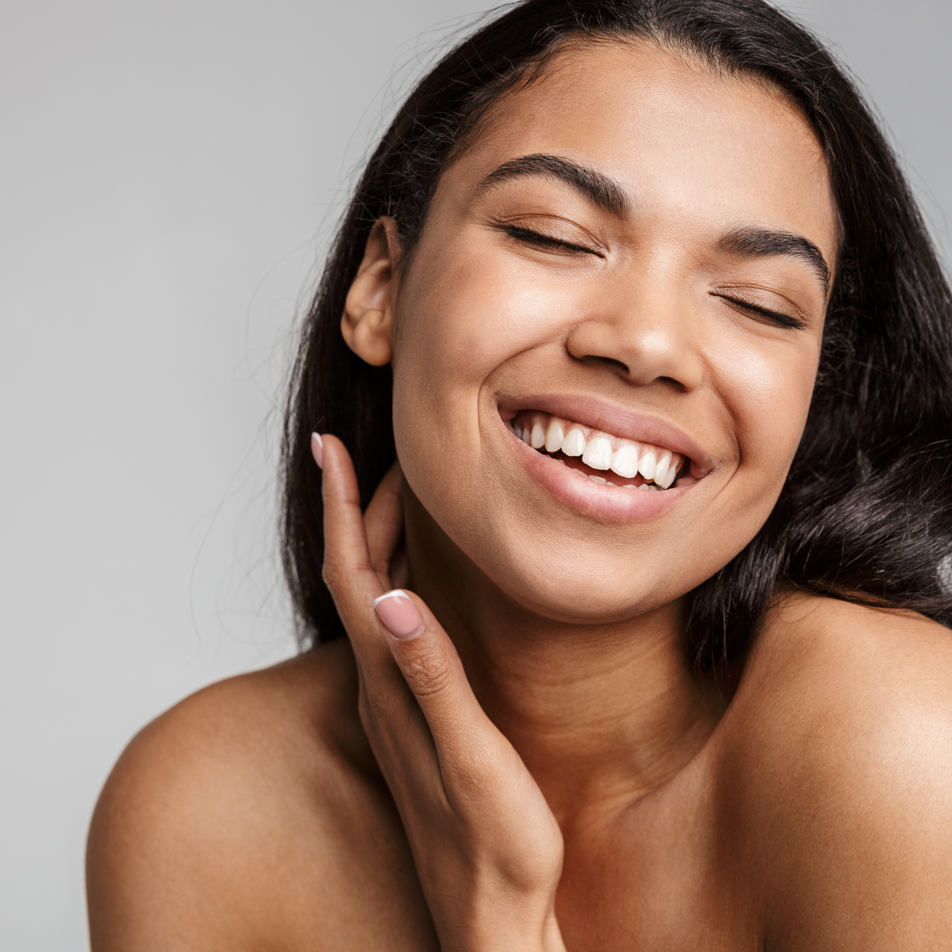A woman is smiling with her eyes closed and her hand on her face.