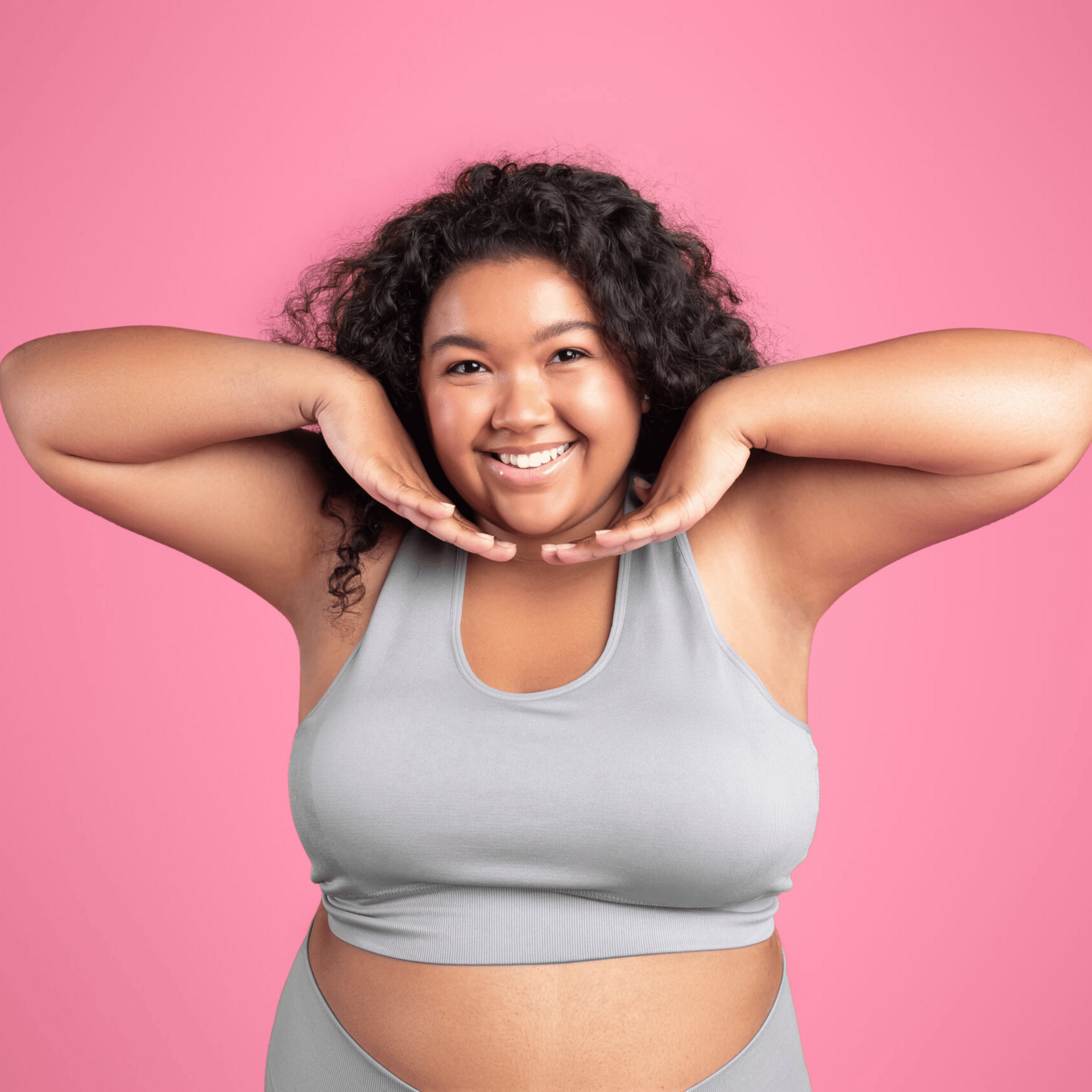 A woman in a crop top and shorts is smiling with her hands on her face.