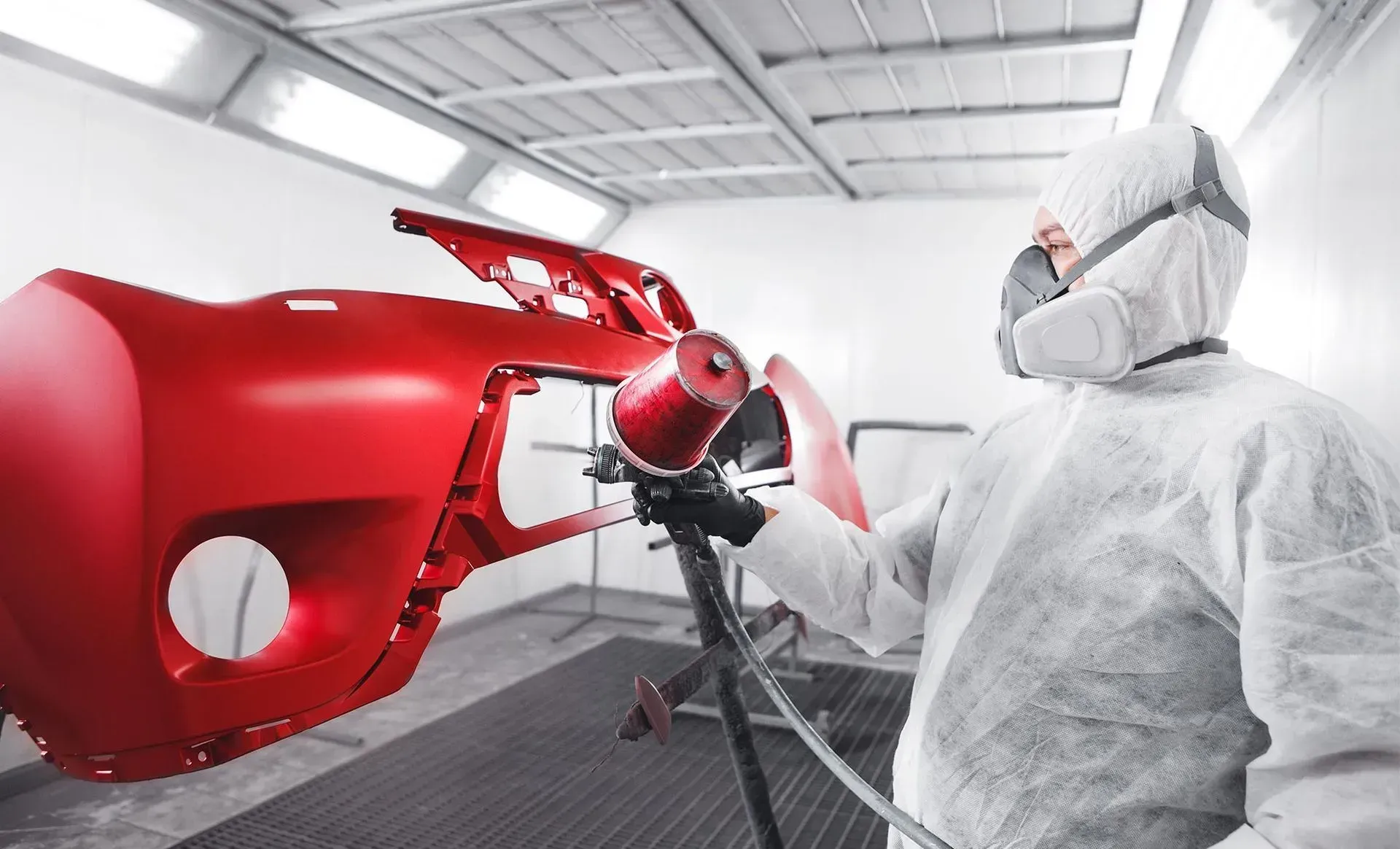 Person in white protective suit spraying red car body in a paint booth