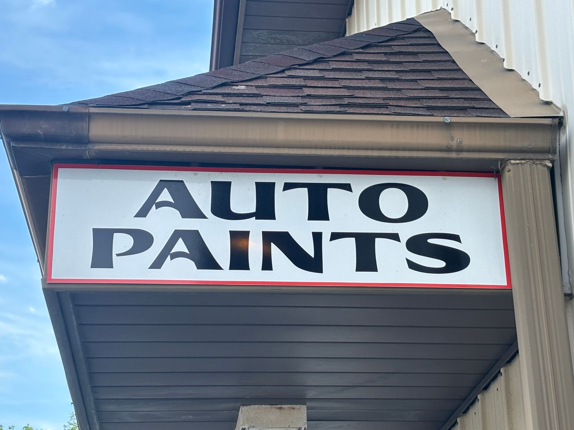 White sign reading “AUTO PAINTS” on a building awning against a blue sky