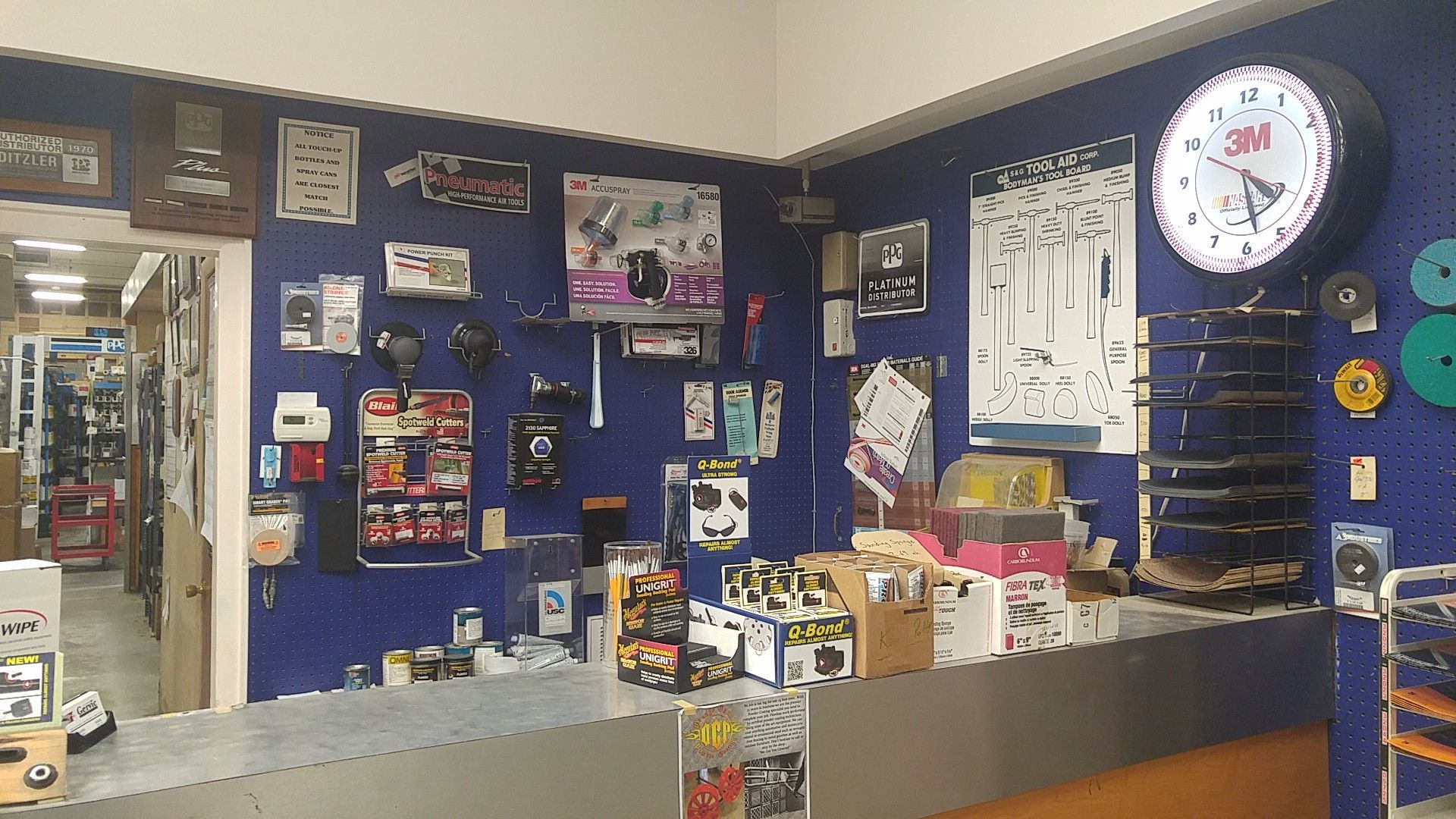 Small retail counter with blue walls, shelves of products, and a large wall clock.