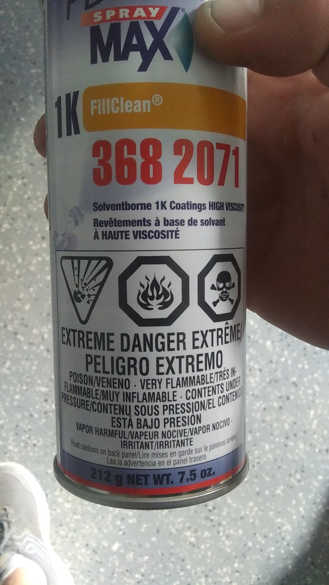 Hand holding a can of Spray Max 2K clear coat with hazard symbols and orange-red label