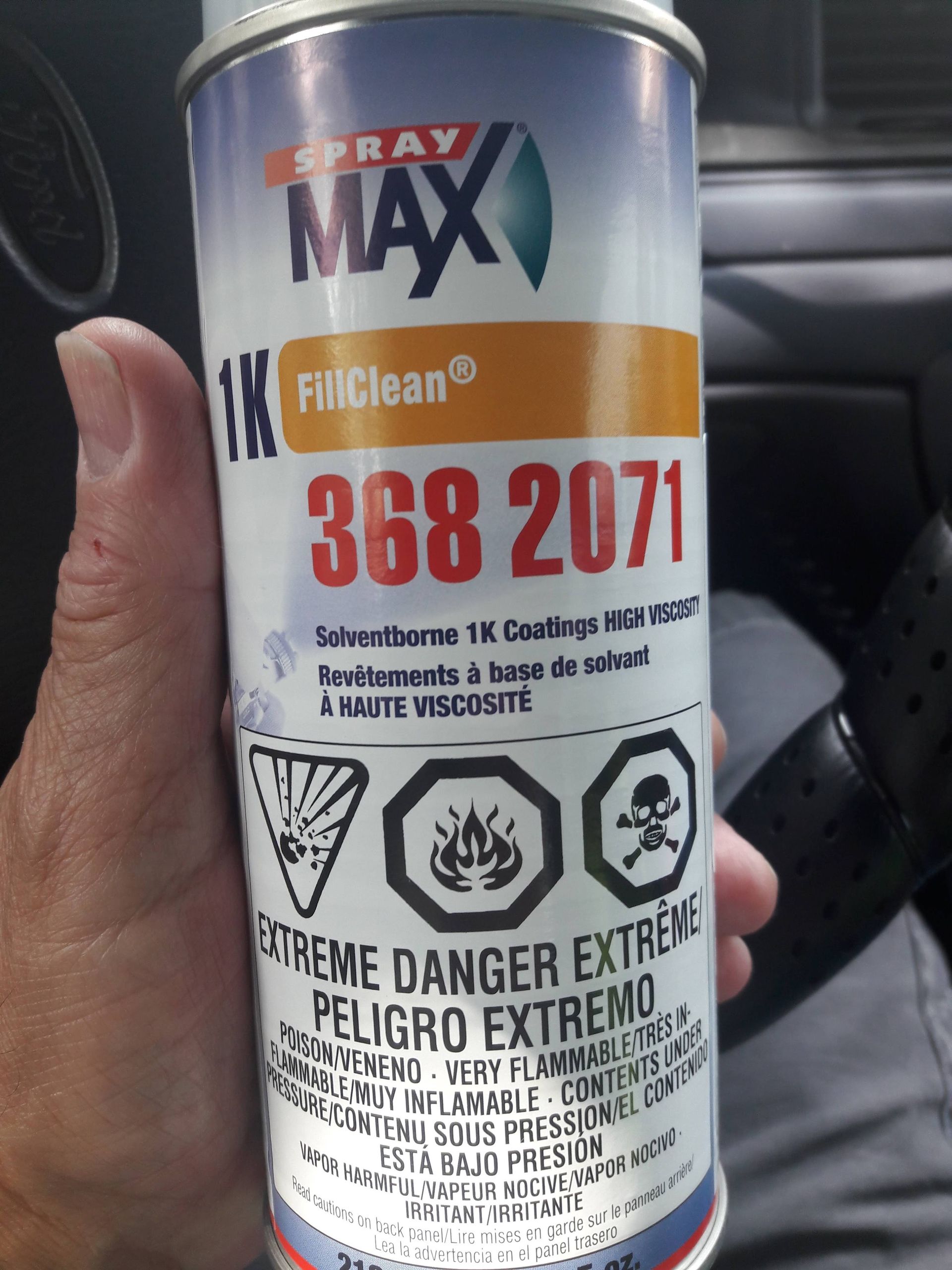Hand holding a gray spray paint can labeled MAX, white and orange, with hazard warning symbols.