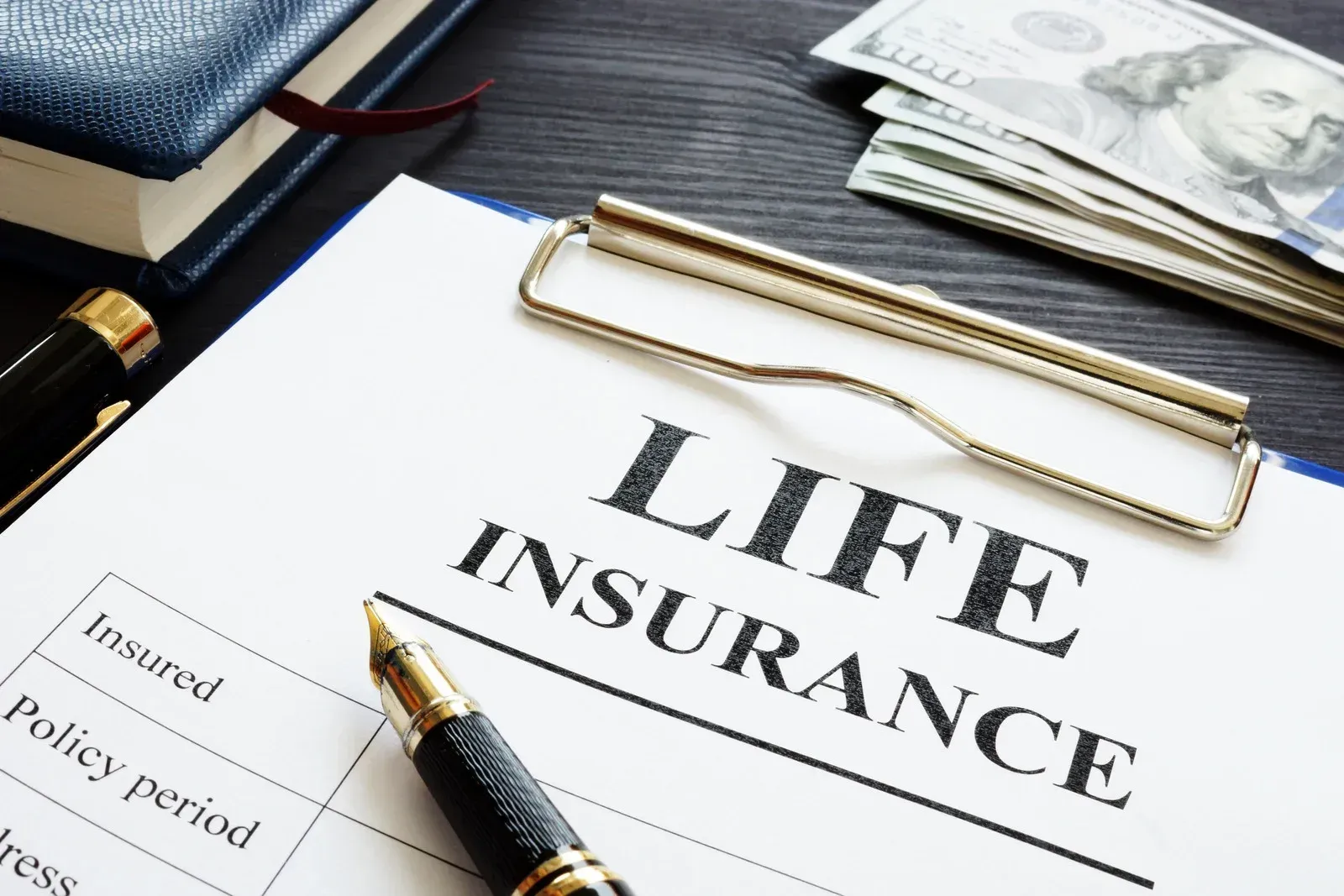 Life insurance form with pen, notepad, money, and pen.