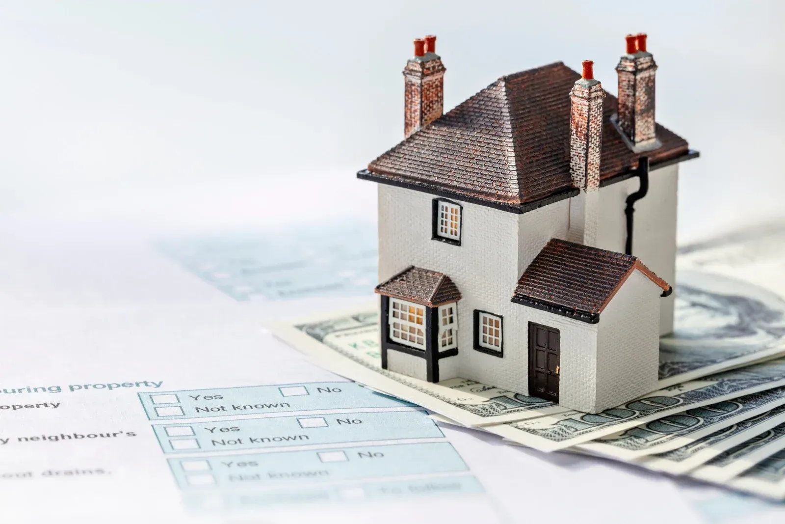 Miniature house on money and paperwork, representing real estate.