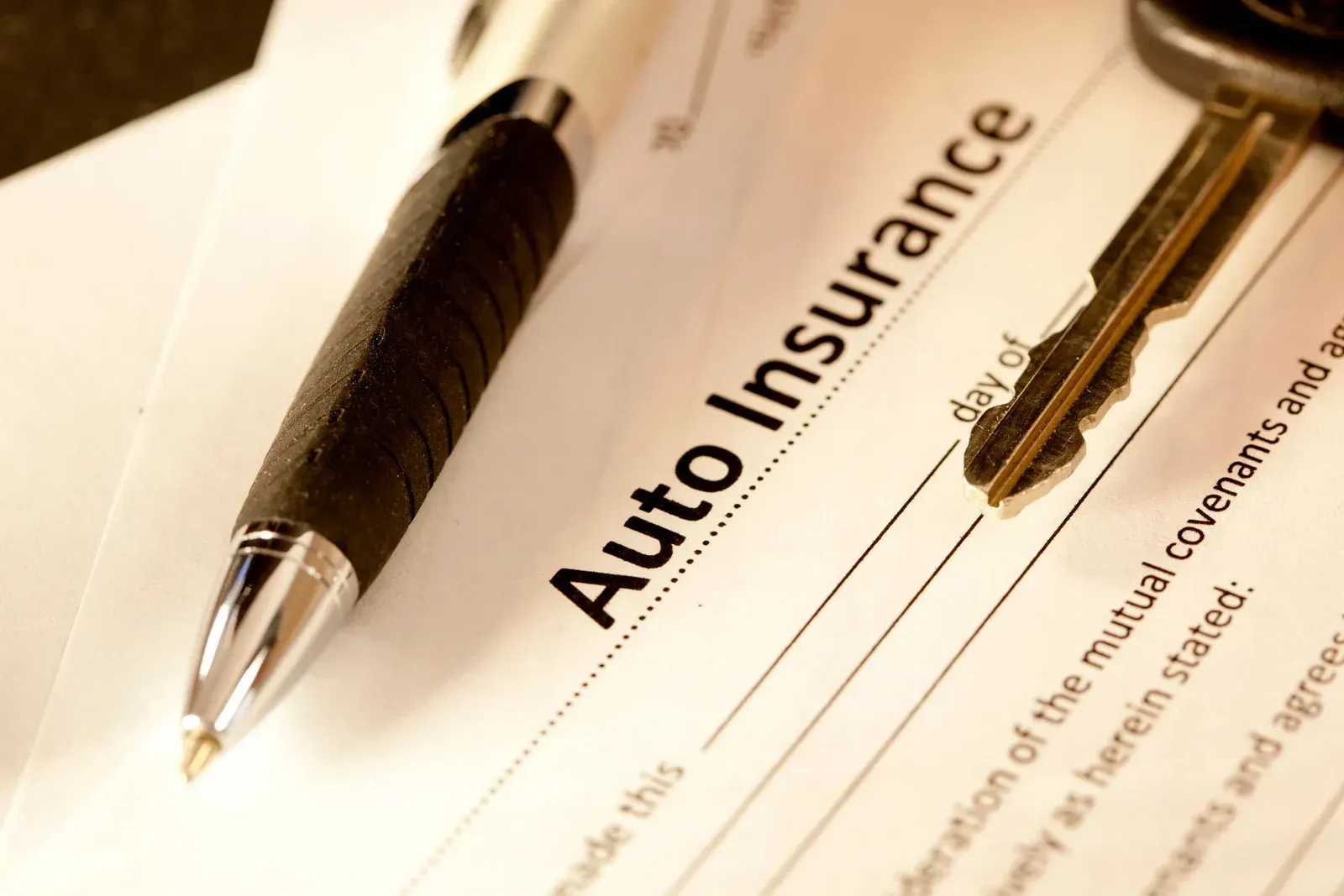 Pen, car key, and auto insurance document.