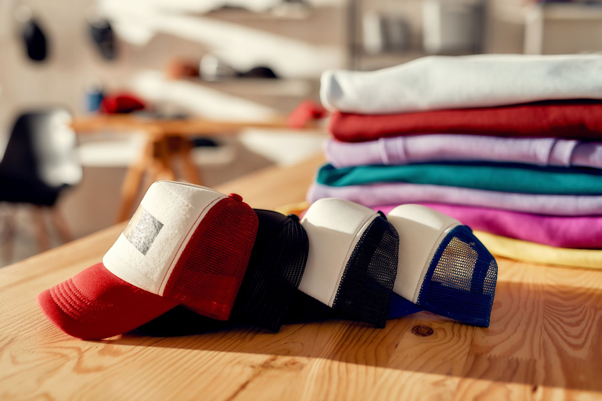 Custom apparel store display with stacked hats and folded t-shirts on wooden table in print shop. Custom apparel store display with stacked hats and folded t-shirts on wooden table in print shop.