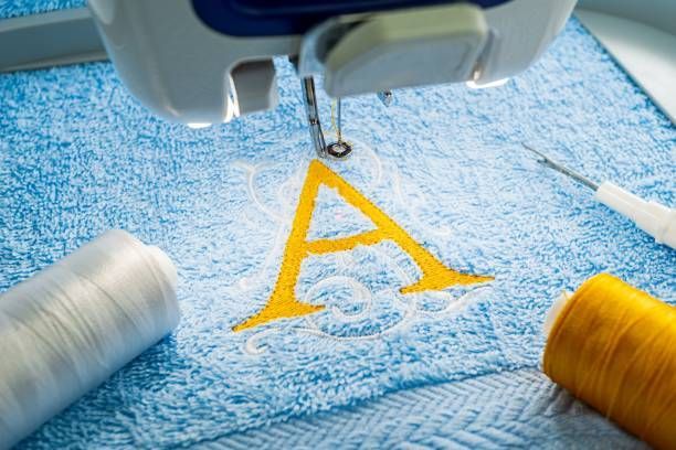 A sewing machine is embroidery the letter a on a blue towel.