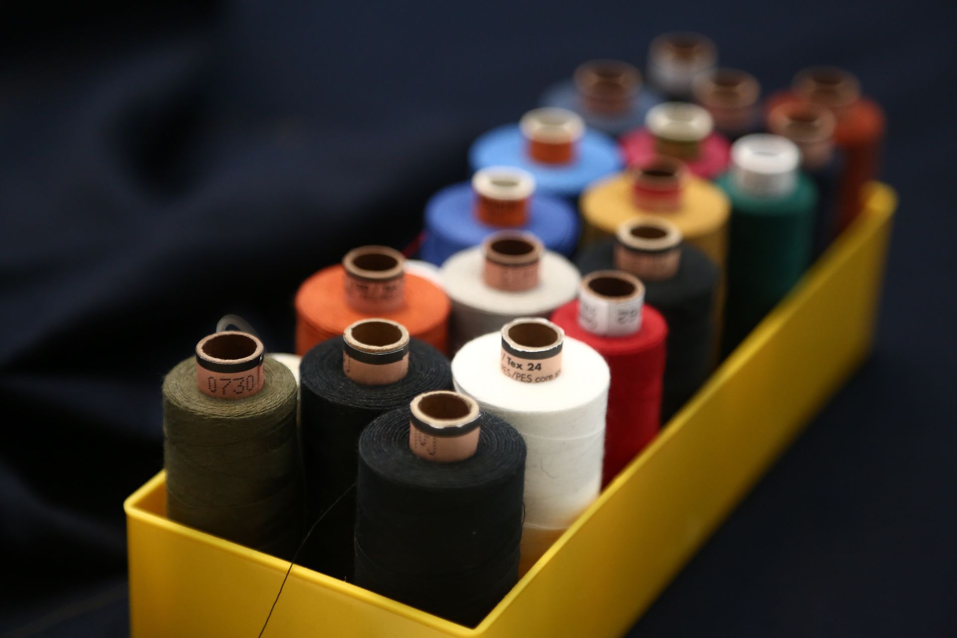 Spools of colorful thread arranged in a yellow box, against a dark blue background. Spools of colorful thread arranged in a yellow box, against a dark blue background.