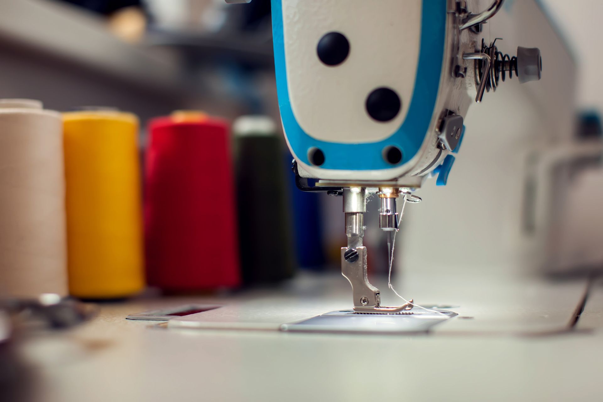 Sewing machine close-up with colorful thread spools in the background.