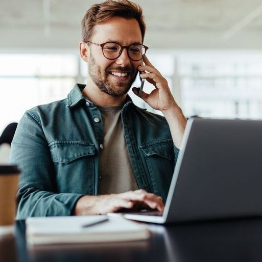 Un uomo parla al cellulare mentre utilizza un computer portatile.