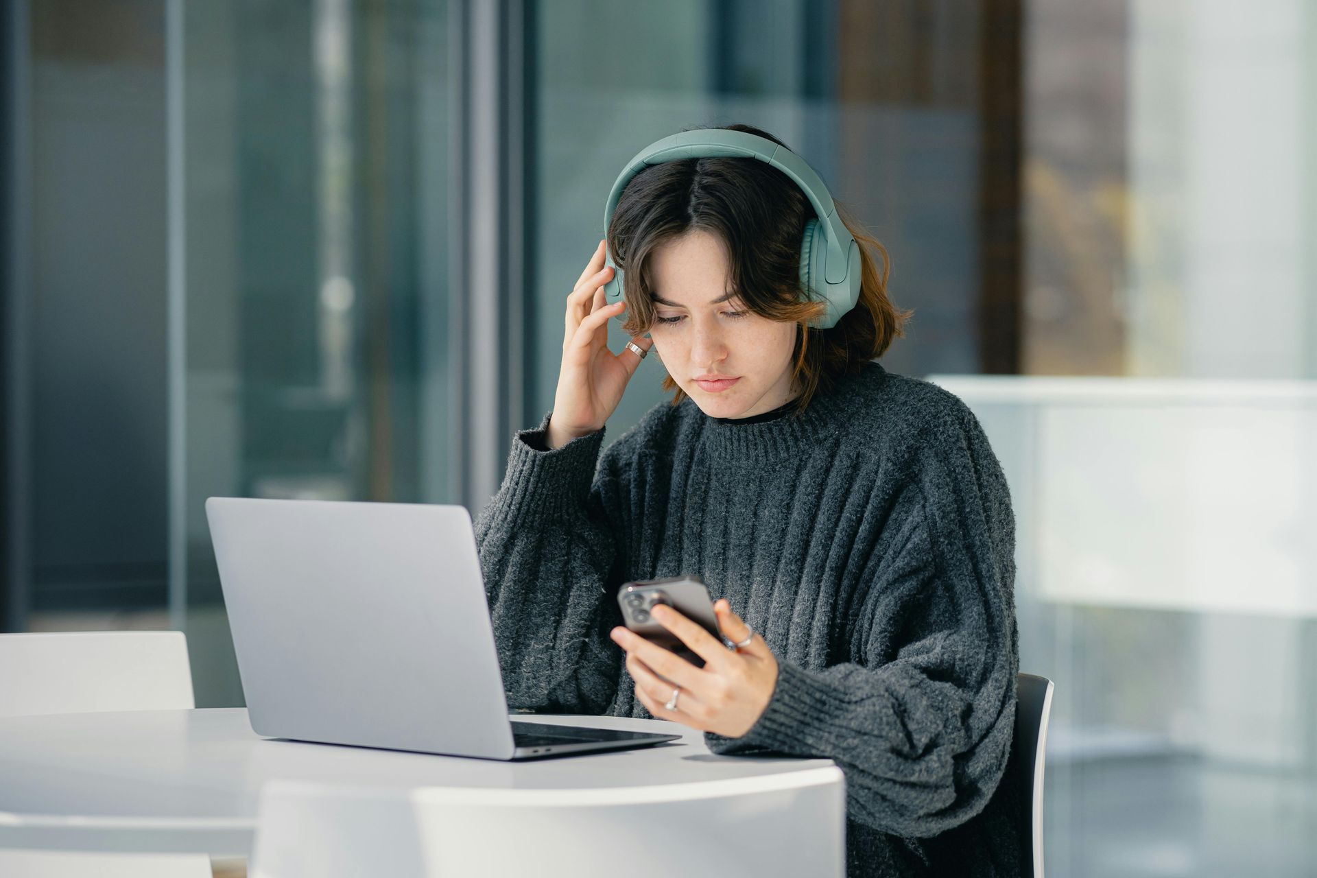 Una donna con le cuffie è seduta a un tavolo con un computer portatile e un cellulare.
