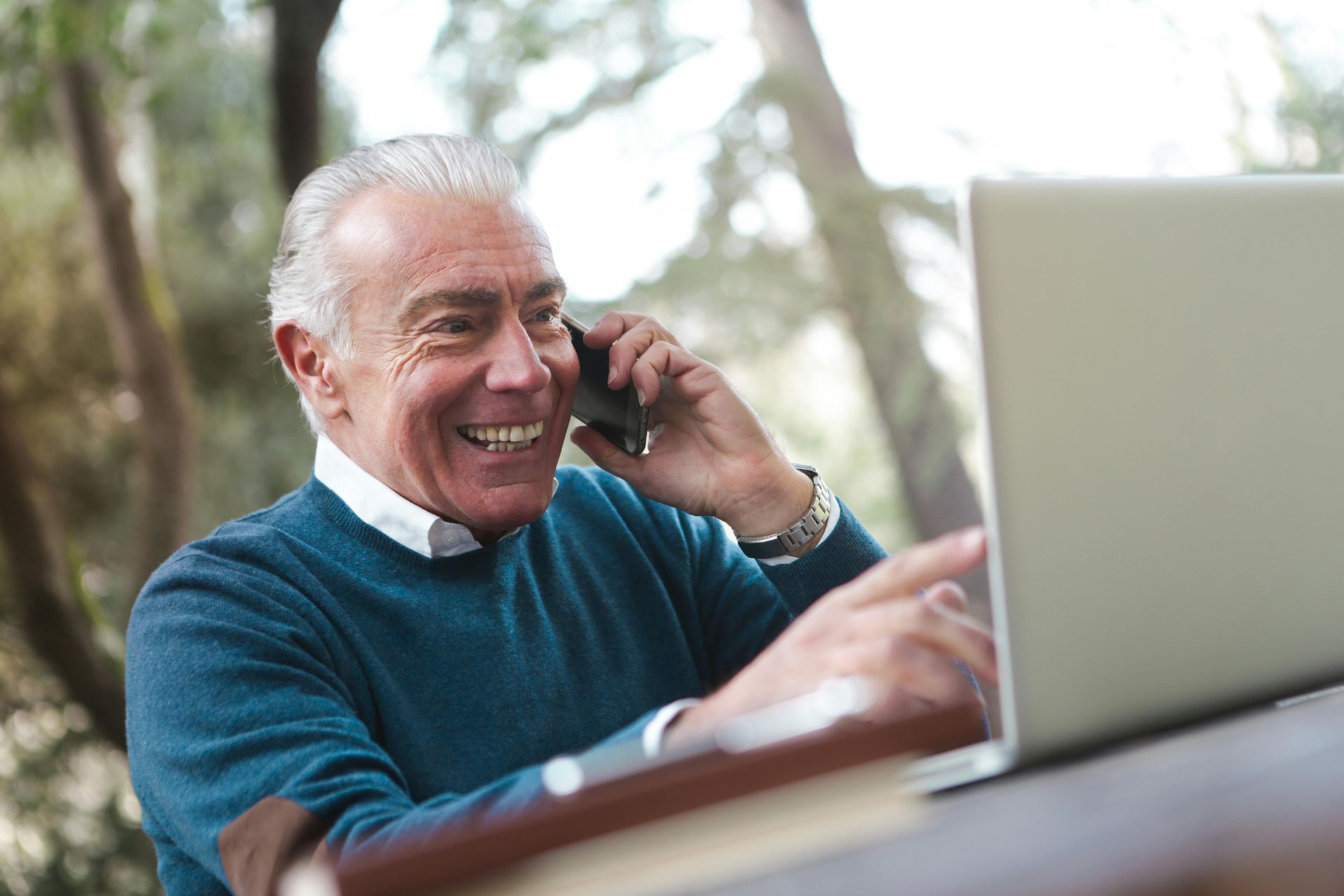 Un uomo anziano parla al cellulare mentre utilizza un computer portatile.