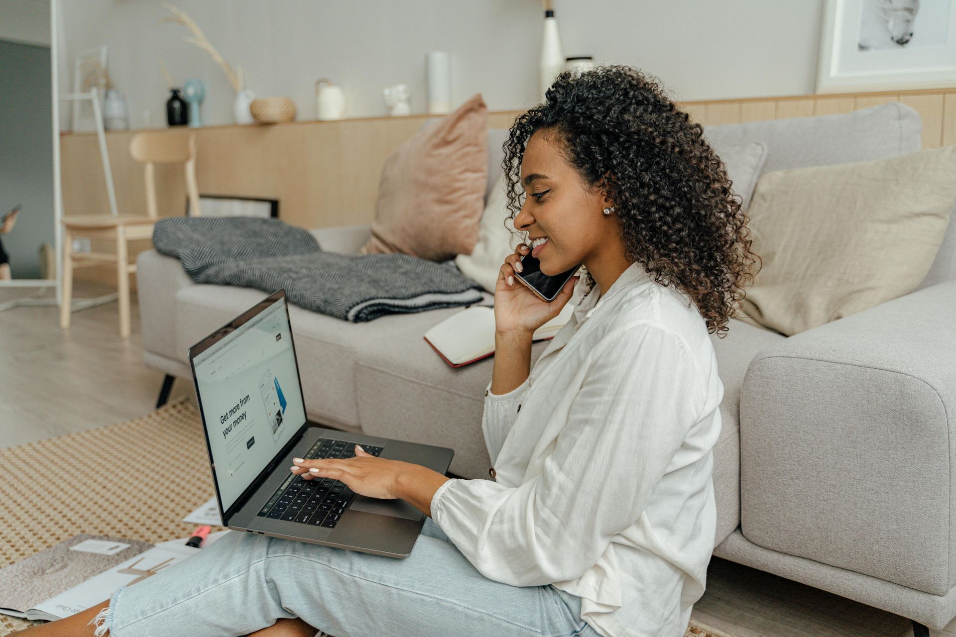 Una donna è seduta sul pavimento e usa un computer portatile mentre parla al cellulare.