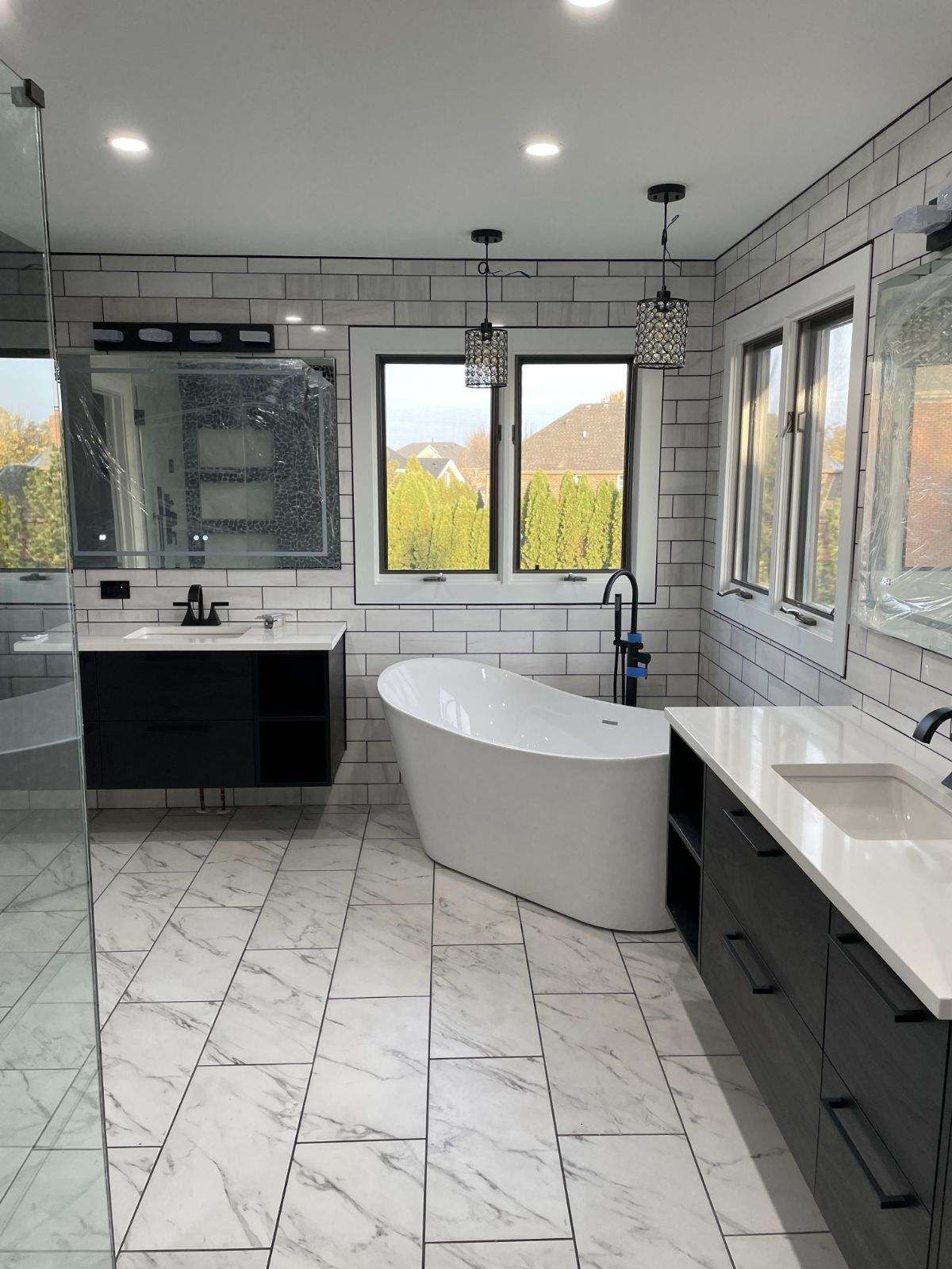 Bright modern bathroom with freestanding tub, large windows, and white tile floor and walls