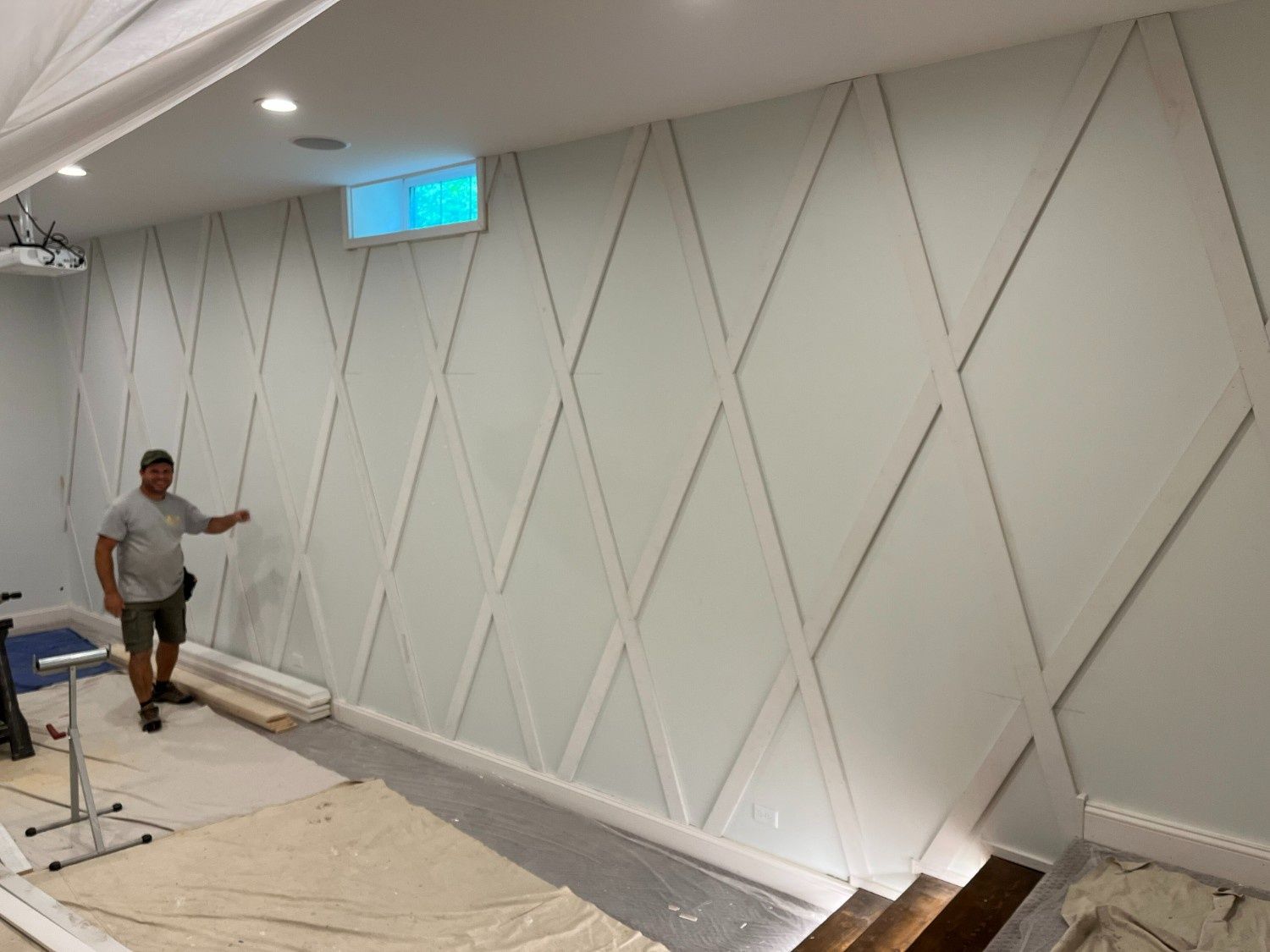 Worker painting a white wall with diamond panel trim in a room under renovation