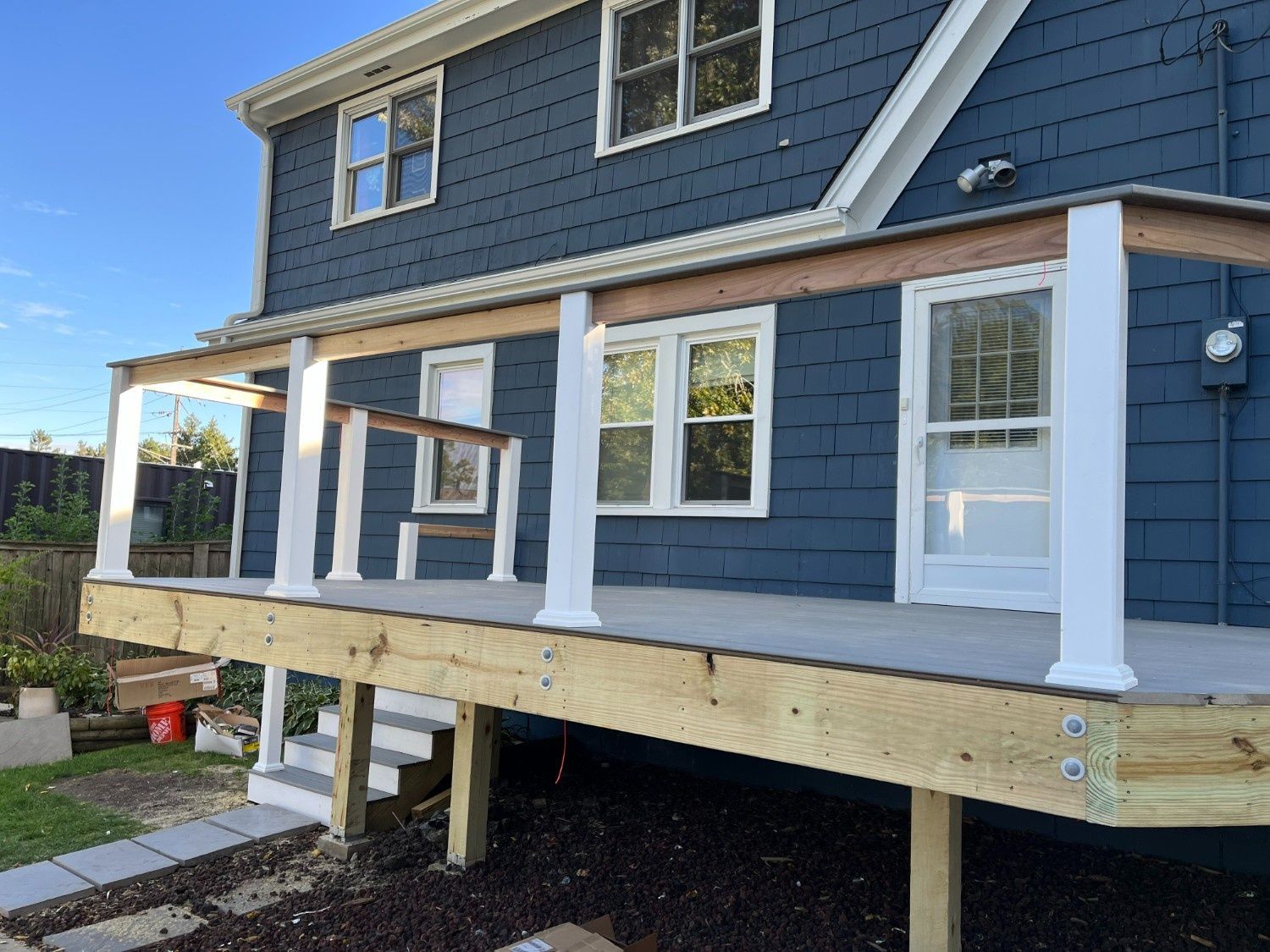 Blue house with a raised wooden deck and white columns on a paved patio.