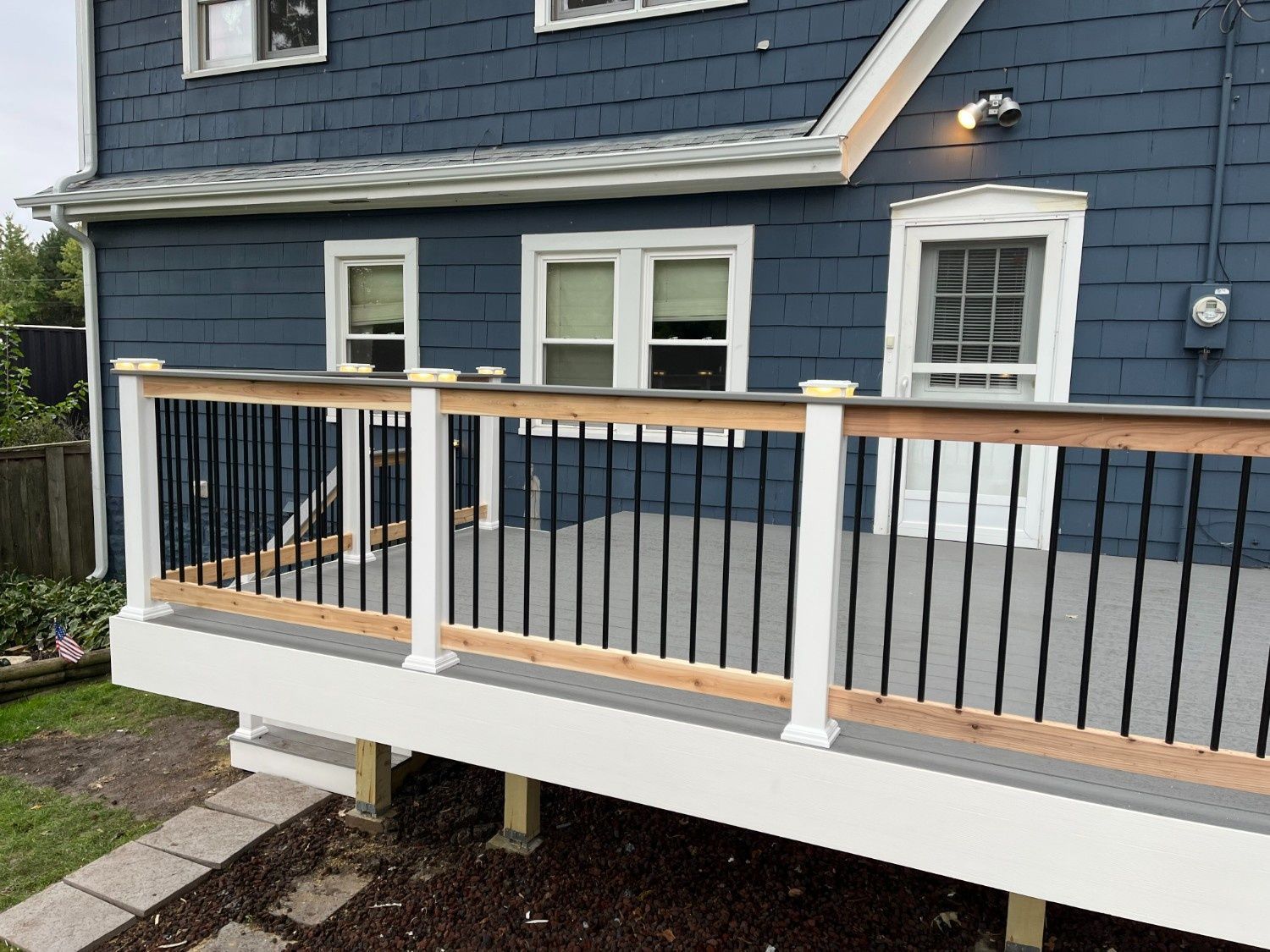 White porch deck with black railings attached to a blue house with white trim.